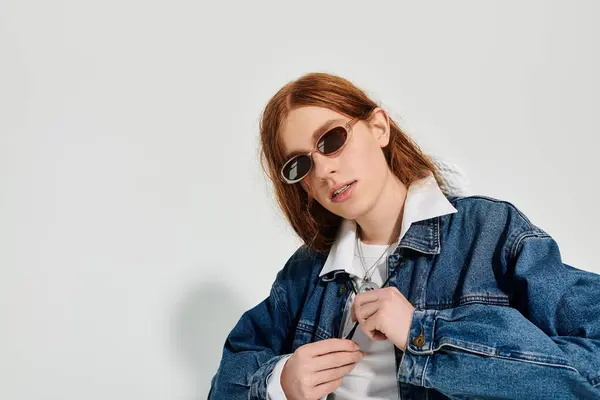 In a modern studio, a teenage boy with long red hair confidently poses in a trendy denim ensemble. — Stock Photo