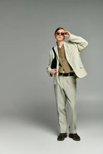 A young man in a stylish outfit stands with poise, showcasing his red hair against a sleek grey backdrop. — Stock Photo