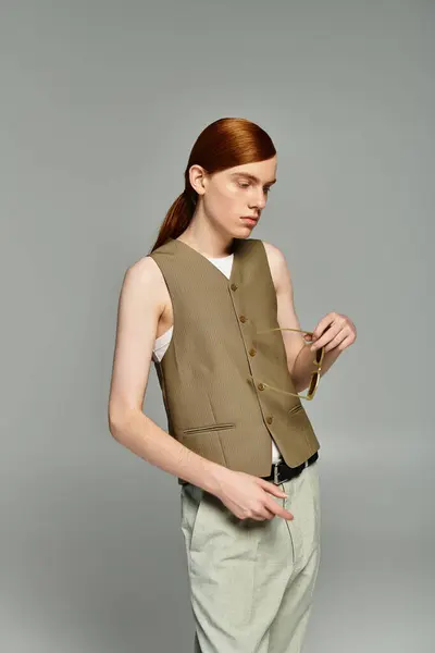 Un adolescent aux cheveux roux saisissants pose en toute confiance dans une élégante tenue décontractée chic sur fond gris. — Photo de stock