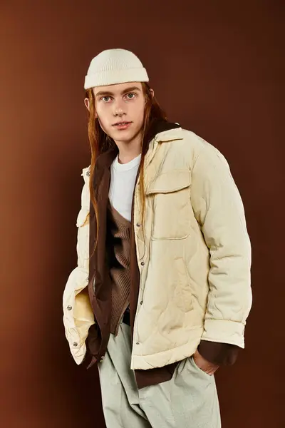 A teenage boy with red hair stands confidently in trendy winter clothing against a warm backdrop. — Stock Photo