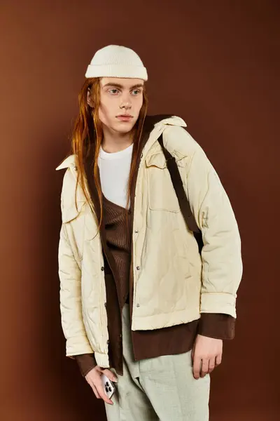 Un adolescent aux cheveux roux se tient en confiance dans un studio, présentant sa tenue à la mode avec un comportement détendu. — Photo de stock
