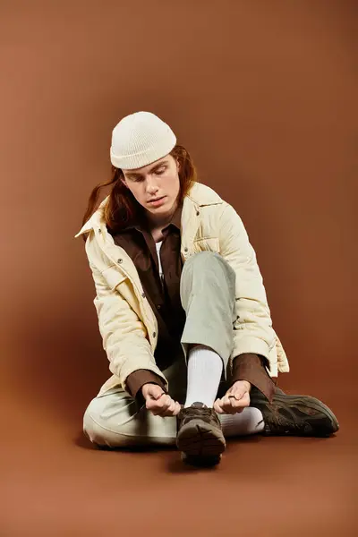 A teenage boy with striking red hair adjusts his stylish shoes while sitting in a studio, surrounded by warm tones. — Stock Photo