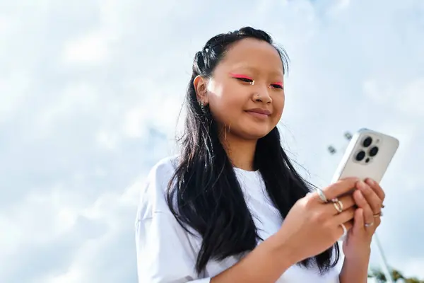 Eine trendige junge Asiatin ist draußen, glücklich mit ihrem Smartphone beschäftigt und umarmt den Tag. — Stockfoto