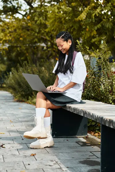 A student girl sits on a bench, focused on her laptop while surrounded by vibrant greenery. — Stock Photo