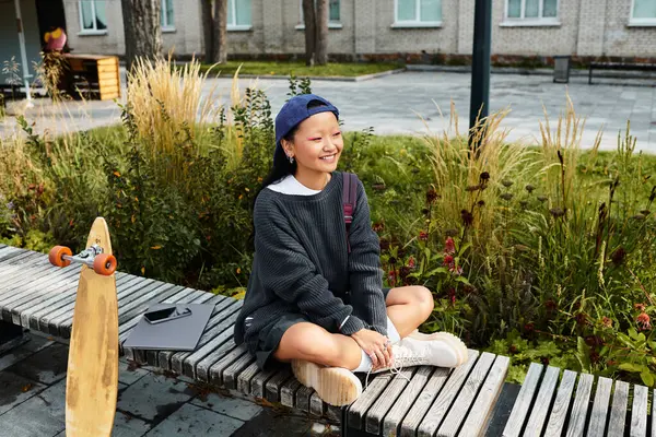 Una giovane ragazza asiatica allegra si siede in un abito elegante, abbracciando la vivace cultura giovanile in un ambiente esterno. — Foto stock