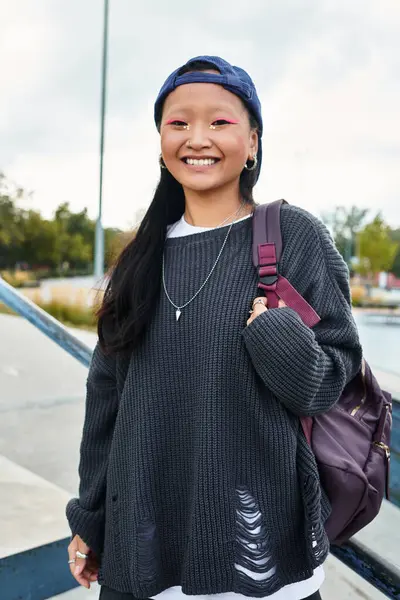 A cheerful young Asian girl in a trendy outfit stands outdoors, radiating joy and style. — Stock Photo