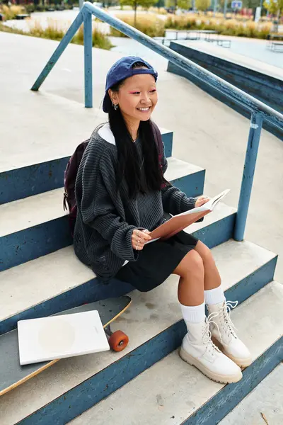 A joyful young student sits on steps, sketching with a skateboard nearby, celebrating youthful creativity. — Stock Photo