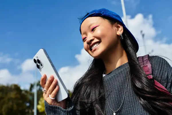 A stylish student girl smiles brightly while texting outdoors, embodying youth and modern culture. — Stock Photo