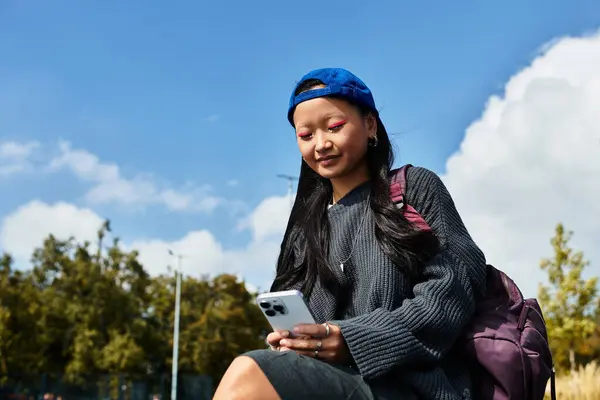 The young student relaxes under a sunny sky, dressed in a fashionable outfit, engrossed in her smartphone. — Stock Photo