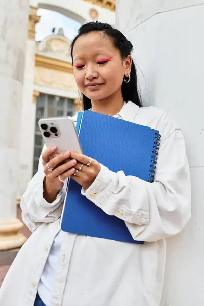 A young student with a trendy outfit engages with her smartphone near the university campus, displaying confidence. — Stock Photo