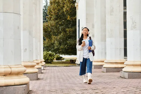 A stylish young Asian student walks confidently between university columns, radiating enthusiasm. — Stock Photo
