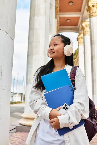 Una estudiante bastante joven lleva sus cuadernos mientras disfruta de un momento fuera en el campus. - foto de stock