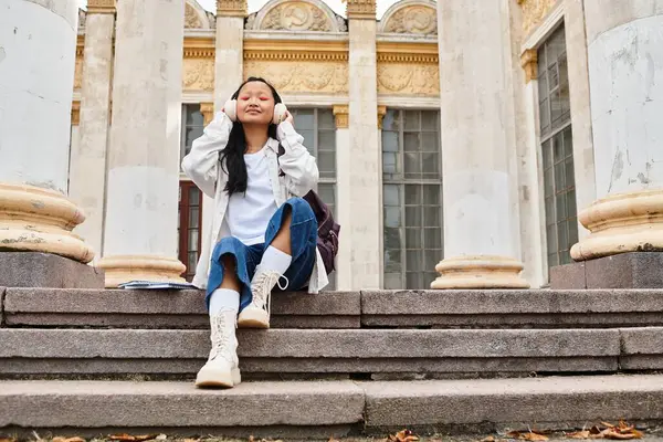 A stylish young student relaxes on university steps, lost in her music and embracing the vibrant campus life. — Stock Photo