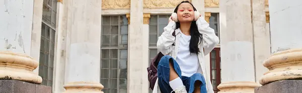 Uma jovem vestida elegantemente relaxa nos degraus da universidade, desfrutando de um momento de tranquilidade e cultura juvenil. — Fotografia de Stock