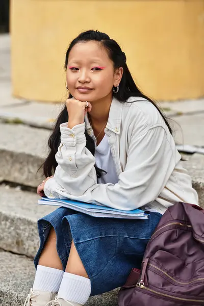 A young Asian student sits on the steps, contemplating her studies while embracing her vibrant style. — Stock Photo