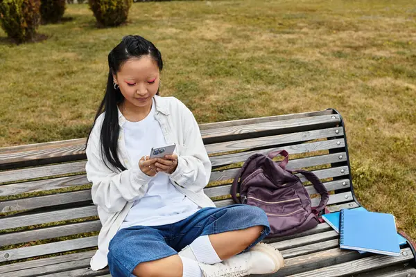 A stylish young woman relaxes on a bench at university, focused on texting her friends in the sun. — Stock Photo