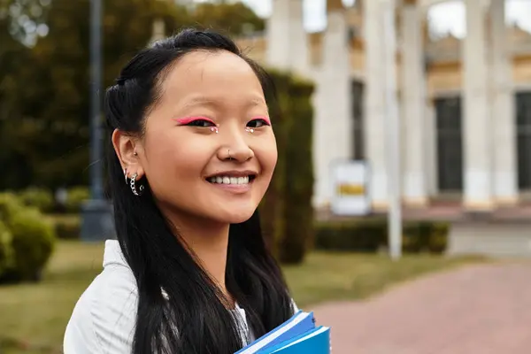 A stylish student smiles confidently while carrying books near her university, embodying diversity and youth. — Stock Photo
