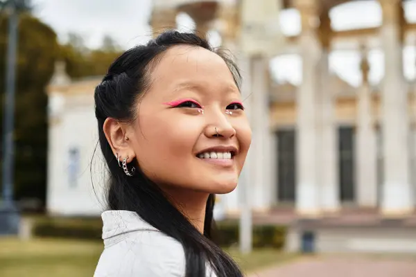 Uma jovem estudante asiática na moda sorri brilhantemente perto de seu campus universitário, abraçando a diversidade e a cultura juvenil. — Fotografia de Stock