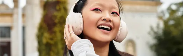 A vibrant young student wears stylish attire while listening to music and smiling on campus. — Stock Photo