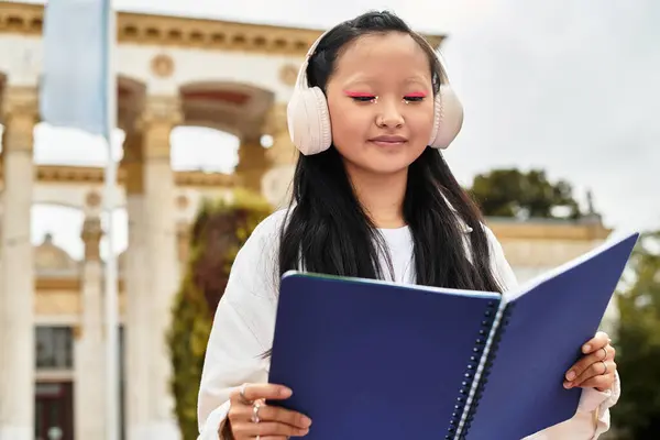 A young student in a trendy outfit studies on campus while wearing headphones, embracing youth culture. — Stock Photo