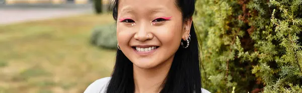 A cheerful young Asian woman in a trendy outfit smiles brightly while standing near her university campus. — Stock Photo