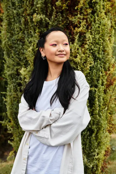 A trendy young Asian student stands confidently near her campus, embracing nature and diversity in youthful culture. — Stock Photo
