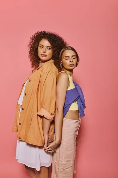 Счастливая лесбийская пара стоит спиной к спине, рука об руку, празднуя любовь на розовом фоне. — стоковое фото