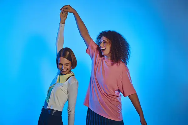 Two happy women highlight their love and joy under vibrant studio lights with a pink backdrop. — Stock Photo