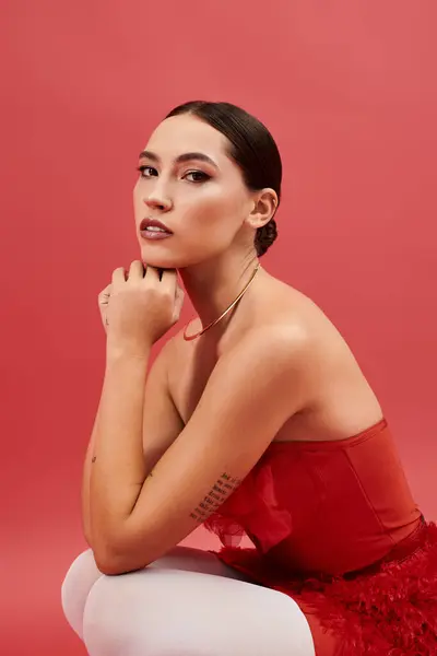 A beautiful girl sits elegantly with a thoughtful expression, wearing a striking red outfit. — Stock Photo