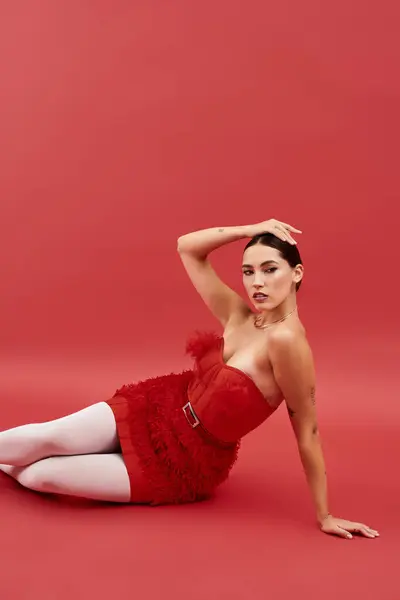 The young woman showcases elegance in a bold red dress, posing confidently on a red backdrop. — Stock Photo