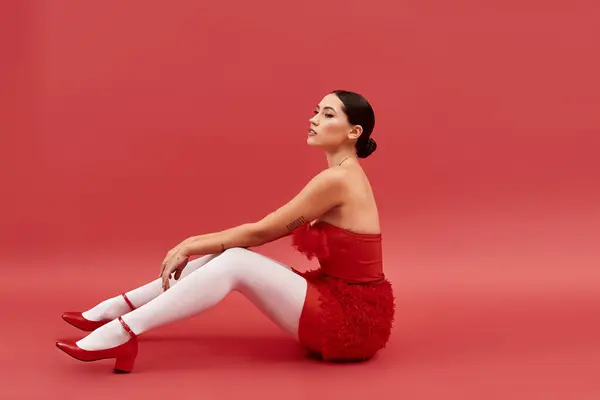 A young woman sits elegantly, showcasing her stylish red attire with confidence and charm. — Stock Photo