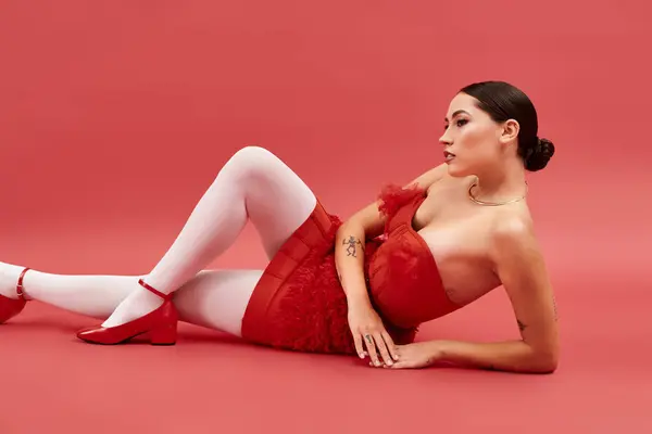 A young beautiful woman reclines elegantly on a bright red backdrop, showcasing her fashion style. — Stock Photo