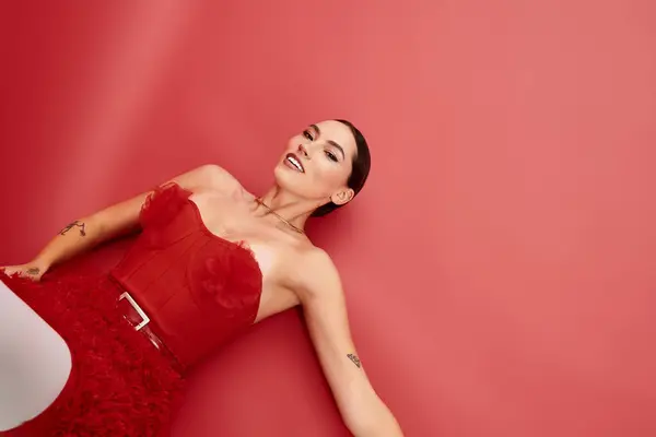 A young beautiful woman showcases elegance in a red dress, lying against a bold backdrop. — Stock Photo