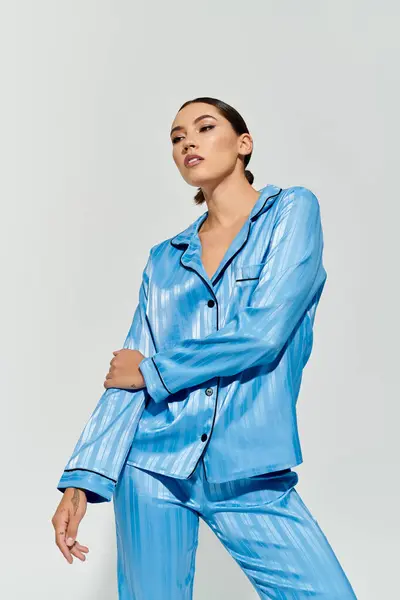 A beautiful young woman showcases her elegance in chic blue pajamas while posing gracefully. — Stock Photo
