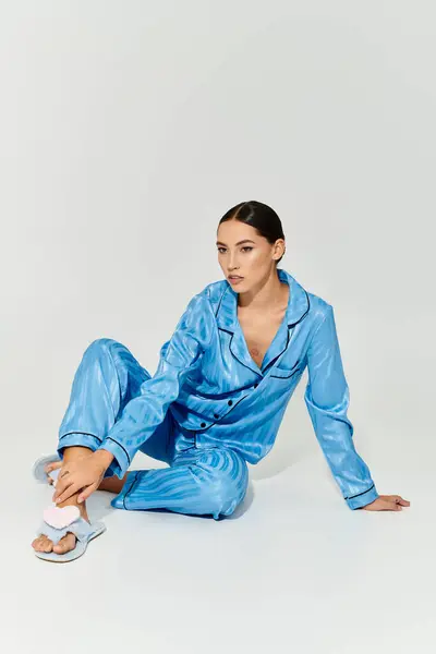 Die schöne Frau sitzt anmutig im trendigen blauen Pyjama mit entspanntem Gesichtsausdruck. — Stockfoto