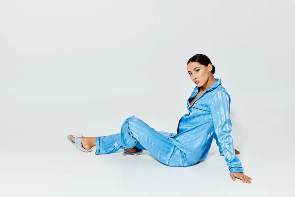 She sits gracefully on the floor, showcasing her trendy blue attire with relaxed elegance. — Stock Photo