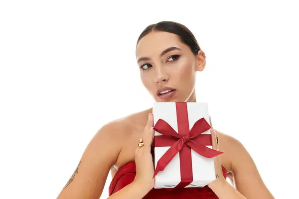 The woman, dressed elegantly, playfully poses while holding a gift with a red ribbon. — Stock Photo