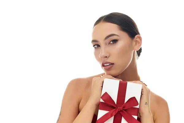 A young woman poses confidently, presenting a wrapped gift adorned with a red bow. — Stock Photo