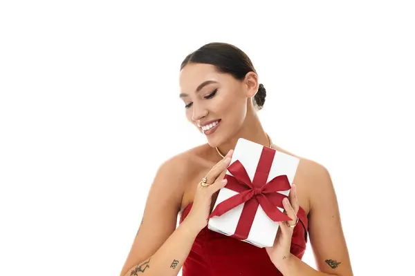 The young woman smiles brightly while holding a gift wrapped in red ribbon, radiating happiness. — Stock Photo