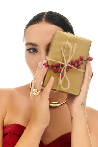This young woman holds a beautifully wrapped gift close to her face, showcasing holiday spirit. — Stock Photo