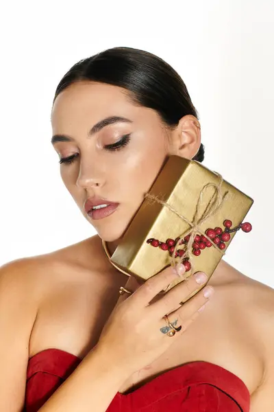 Una joven con un peinado elegante abraza suavemente un impresionante regalo de oro adornado con bayas. - foto de stock
