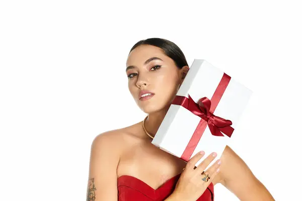 A young, beautiful woman in elegant attire poses confidently while showcasing a gift box. — Stock Photo