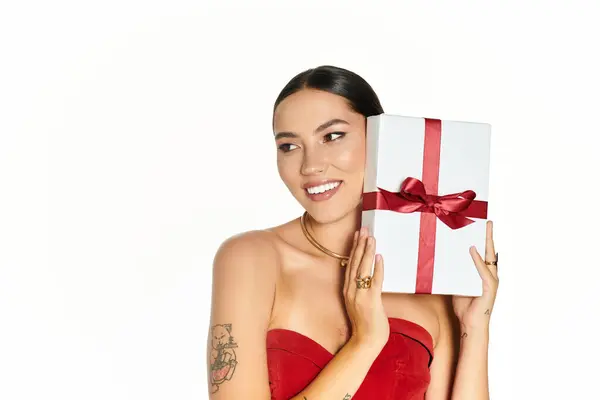 This young woman looks delighted while presenting a lovely gift adorned with a red ribbon. — Stock Photo