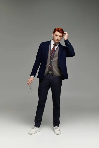 A young, handsome student in a layered winter outfit poses confidently in a studio while adjusting his hair. — Stock Photo