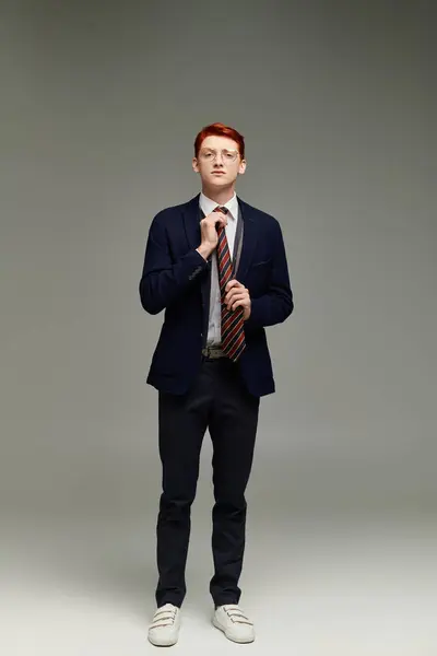 Un joven elegante con el pelo rojo ajusta su corbata, encarnando la sofisticada moda invernal en un estudio. - foto de stock