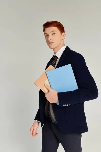 A well-dressed student with red hair confidently holds colored folders in a chic studio environment. — Stock Photo