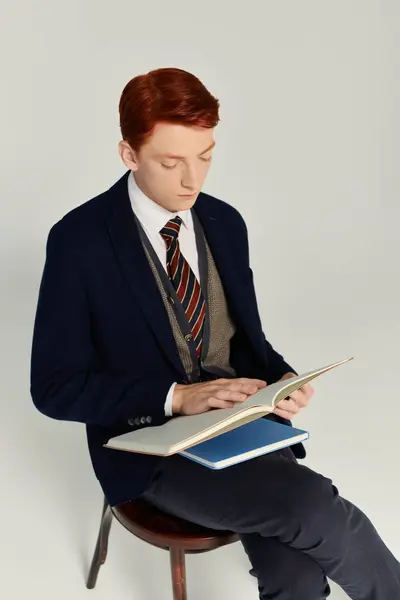 Un jeune homme aux cheveux roux saisissants absorbé par la lecture alors qu'il était habillé dans un ensemble d'hiver à la mode. — Stock Photo