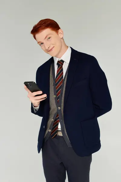A confident young man with red hair showcases a fashionable winter outfit while using his smartphone. — Stock Photo