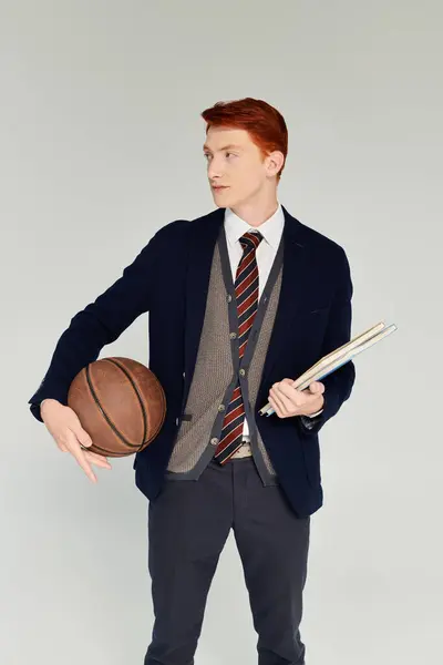 A handsome student with striking red hair showcases a chic winter ensemble while holding a basketball and books. — Stock Photo