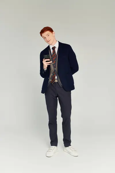 Un estudiante de moda se pone de pie con confianza en un traje de capas elegantes mientras revisa su teléfono. - foto de stock